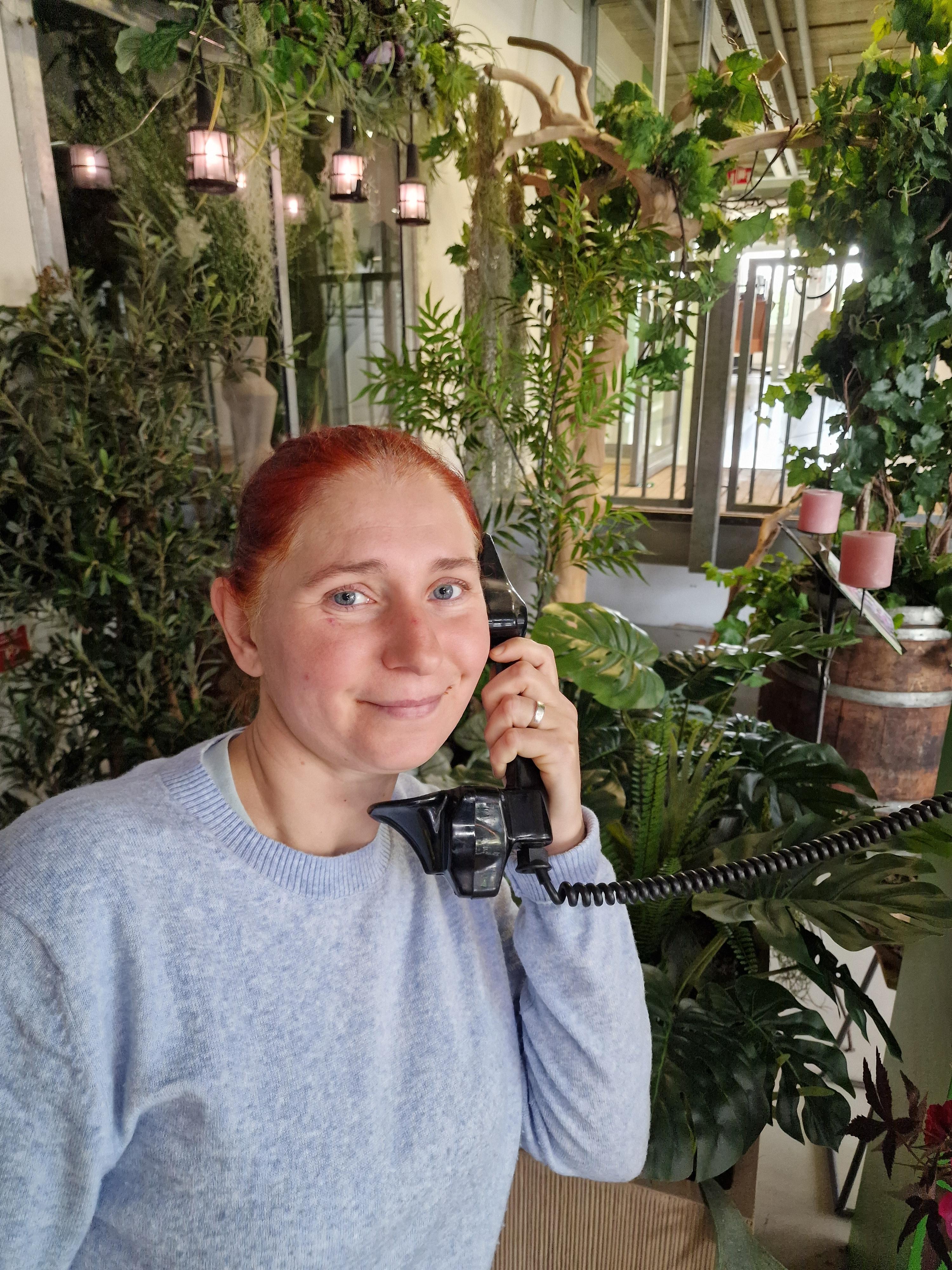 Mevrouw met een vaste telefoon in der hand met op de achtergrond veel planten